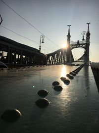 Silhouette bridge over street against sky during sunset