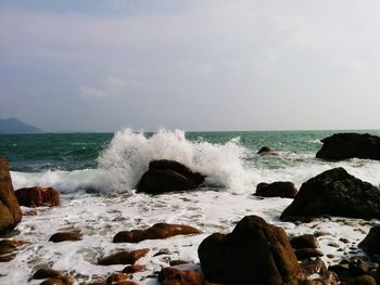 Waves splashing on rocks in sea against sky