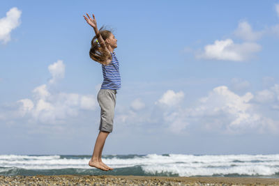Side view of girl jumping at beach against sky