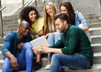 Low angle view of friends using digital tablet while sitting on steps