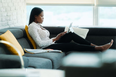 Full length of businesswoman using laptop sitting on sofa at home