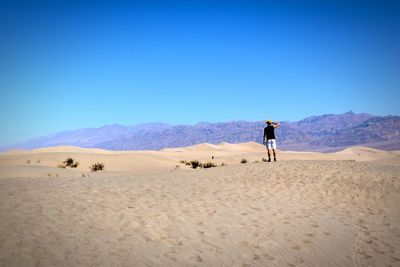 Rear view of man standing at desert against clear sky during sunny day