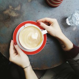 Cropped hands of woman holding coffee cup on table