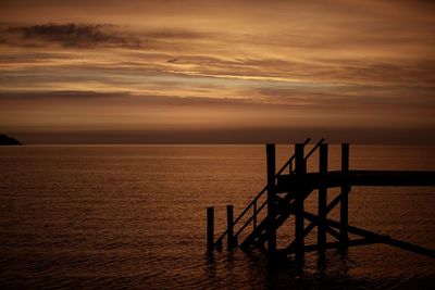 Silhouette structure in sea against cloudy sky