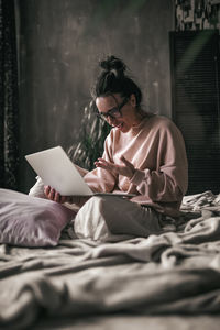 Young woman sitting on bed at home