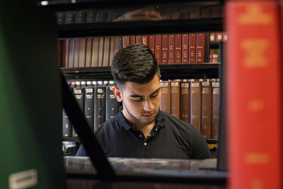 Young man seen through bookshelves at college library