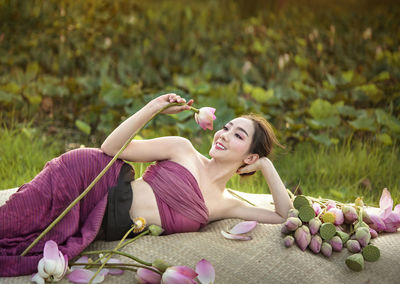 Beautiful woman resting on textile with lotus flowers on land
