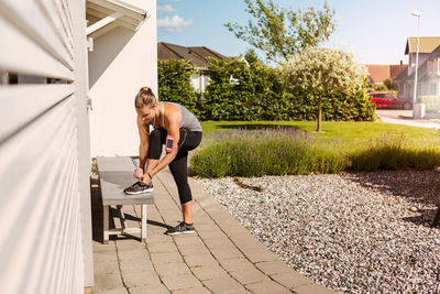 Full length of woman tying shoes on bench in backyard during sunny day