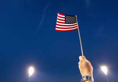 Close-up of man holding american flag against blue sky