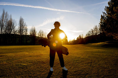 Rear view of man standing on field against sky during sunset