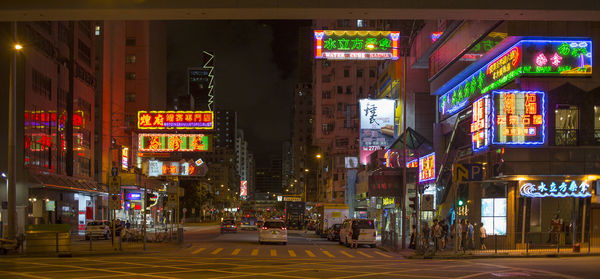 Illuminated street amidst buildings in city at night, hong kong