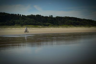 Man cycling at beach against sky