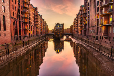 Reflection of buildings on bridge against sky during sunset