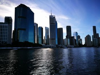 Modern buildings by river against sky in city