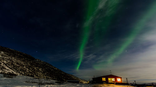 Illuminated house by mountain during aurora borealis