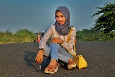 Portrait of young woman sitting on road against trees