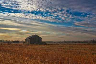 Barn at agricultural field against cloudy sky during sunset