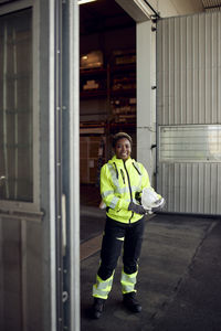 Portrait of smiling young female blue-collar worker in workwear standing in factory