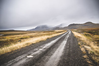 Road leading towards mountains against sky