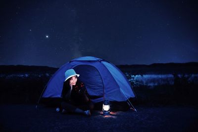 Man sitting in tent against sky at night