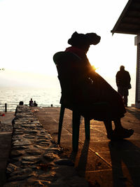 Silhouette man sitting on beach against sky