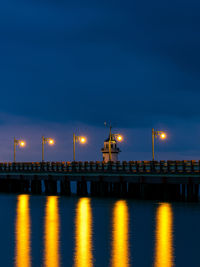 Illuminated bridge over river against sky at night