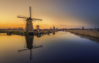 Traditional windmill by river against sky during sunset