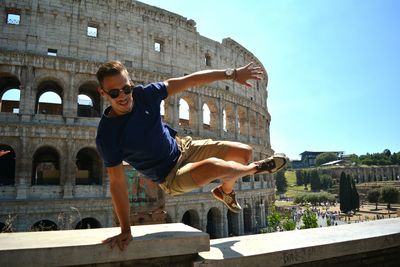 Low angle view of man jumping in city against blue sky