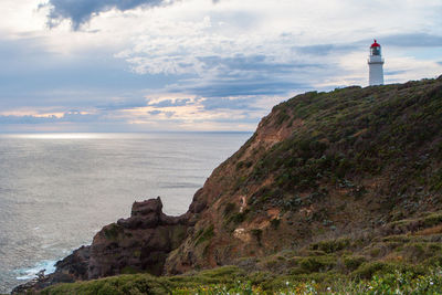 Lighthouse on rock by sea against sky