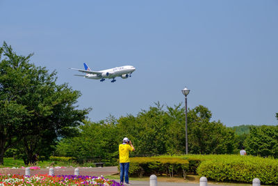 Rear view of man with airplane flying against clear blue sky