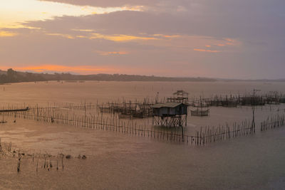 Wooden posts in lake against sky during sunset