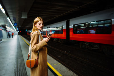 Portrait of young woman using mobile phone at railroad station