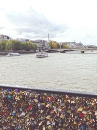 Padlocks on bridge over river against sky in city