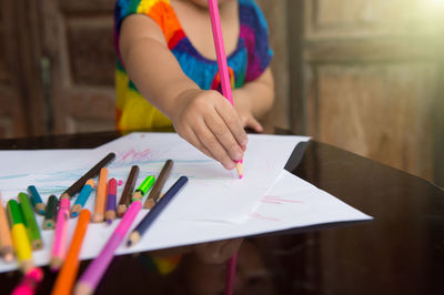 Midsection of person holding paper with colored pencils on table