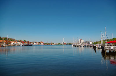 Boats moored at harbor against clear blue sky