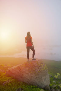 Rear view of woman walking on beach against sky during sunset