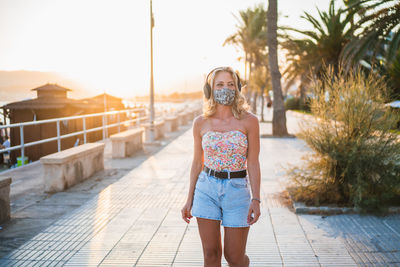 Young woman wearing flu mask walking on street against sky