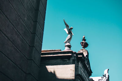 Low angle view of statue against building against clear blue sky