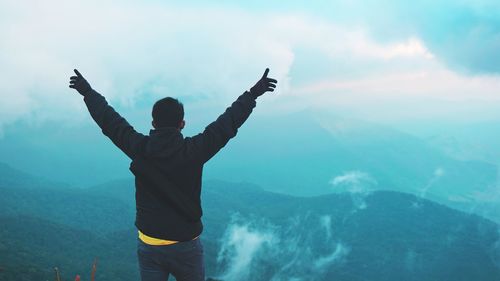 Man with arms raised standing against mountains