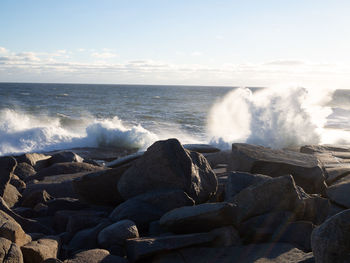 Waves splashing on rocks at shore against sky