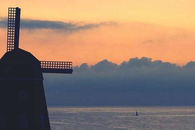 Silhouette traditional windmill by sea against sky during sunset