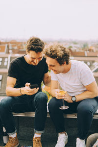 Man showing mobile phone to friend having drink at terrace during party