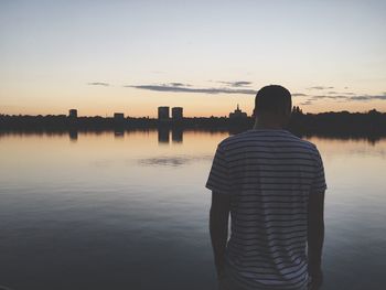 Rear view of silhouette woman standing by river against sky during sunset