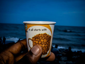 Close-up of hand holding food by sea against sky