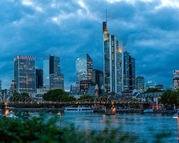 Modern buildings by river against sky in city