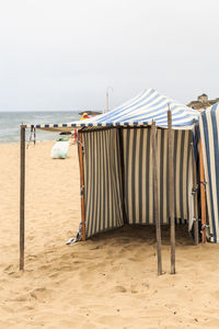 Hooded chairs on beach against sky