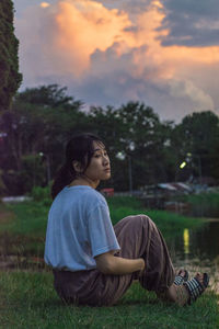 Young woman sitting by lake during sunset