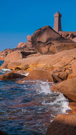 Lighthouse on cliff by sea against clear blue sky