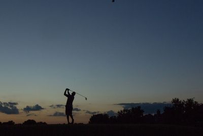 Silhouette man playing golf course on field against sky during sunset