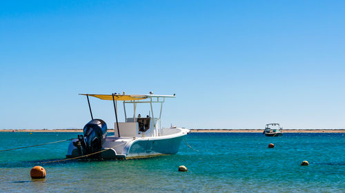 Boats moored in sea against clear blue sky